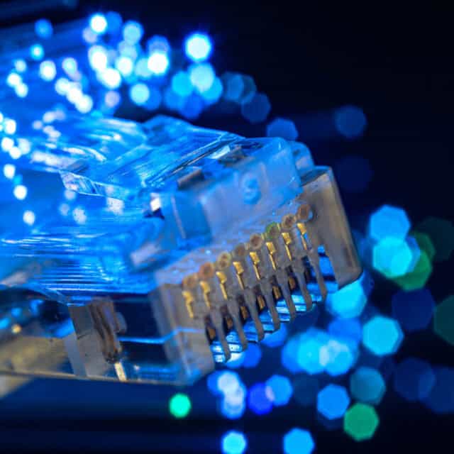 Close-up of an ethernet cable connector with glowing blue fiber optics and a blurred background, showcasing advanced networking technology.