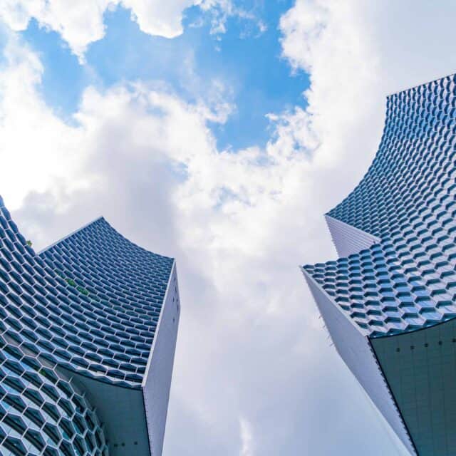 Low-angle view of two modern skyscrapers with unique, textured facades under a sky suggestive of cloud technology.