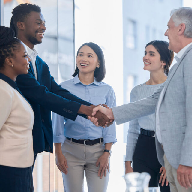Diverse group of sales engineering professionals greeting each other with handshakes and smiles in a modern office setting.