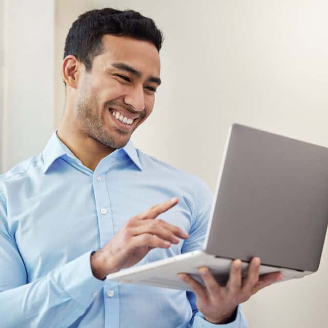 A smiling man holding and interacting with GeoQuote on a laptop in a bright indoor setting.