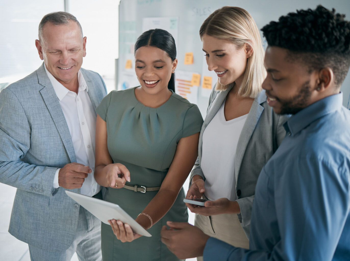 Four diverse professionals engaging with a digital tablet and discussing cloud technology in a bright office setting.