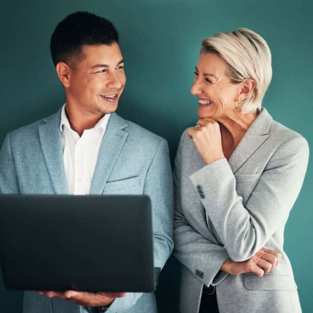 Two business professionals, a man and a woman, smiling and looking at each other, holding a laptop together against a dark green background. This description is too vague and lacks specific context or details that typically