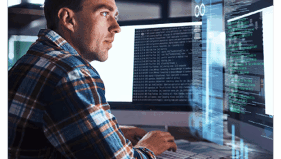 A man in a plaid shirt sits at a desk, focused on multiple computer screens displaying lines of code and data related to cybersecurity in a dimly lit, modern workspace.
