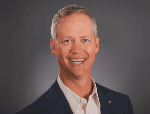 Smiling man with short gray hair, wearing a dark suit jacket and white shirt, poses in front of a plain gray background—perfect for your 2025 Year in Review or Technology Advisor Enablement materials.