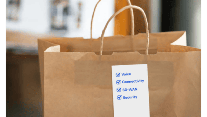 A brown paper shopping bag with a label attached, displaying a checklist with blue checkmarks next to Voice, Connectivity, SD-WAN, and Security—ideal for SMB self-service advisors. Another bag is visible in the background.