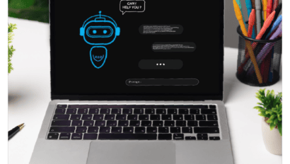 A laptop on a white desk displays a chatbot interface featuring SMB self-service advisors with a robot icon and the text "CAN I HELP YOU?" A container of colorful pens and a small plant are visible in the background.