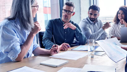 Four colleagues sit around a conference table during a meeting, reviewing documents and discussing their network service.